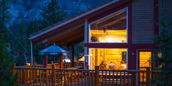 Cozy mountain cabin accommodation in Banff with warm lighting, surrounded by evergreen trees and Rocky Mountain views. HI Hostels is the ideal base for Western Canada Rockies Adventure Tours.