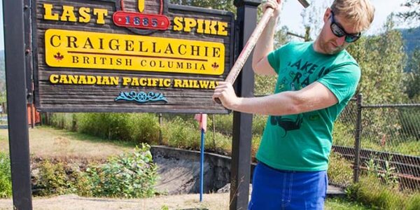 Man with pickaxe outside Craigellachie Village sign in Revelstoke, Rockies