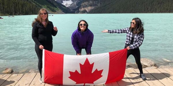 Three women holding Canadian flag at Lake Louise viewpoint with Victoria Glacier in background